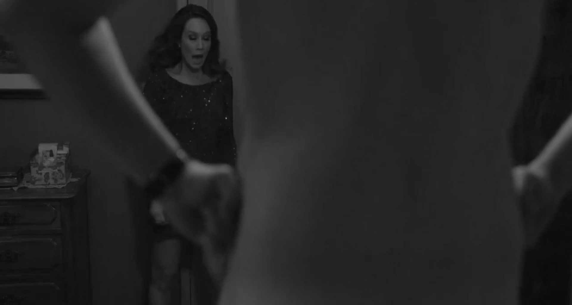 Imagem em preto e branco de homem nu, de costas, em primeiro plano. Ao fundo, uma mulher olha surpresa para a cena. 